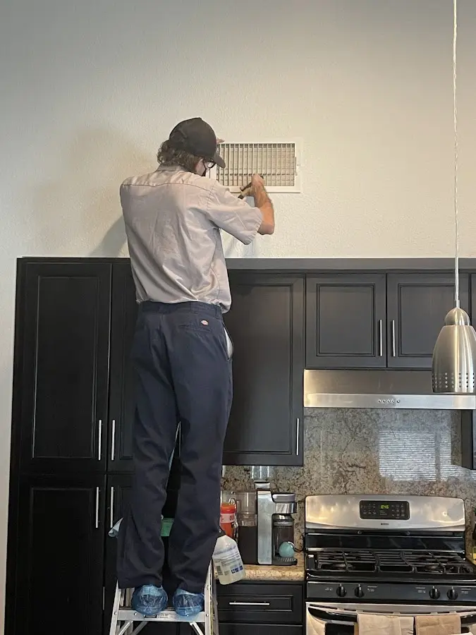 Technician inspecting an air vent during HVAC service in Troy